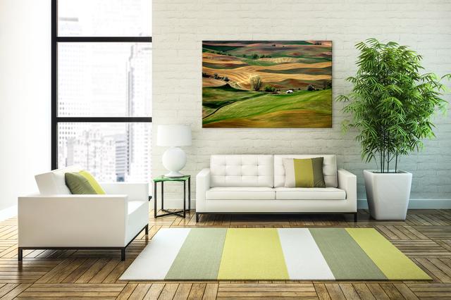 large wall art display of country side artwork on  a brick wall in living room with couch and arm chair